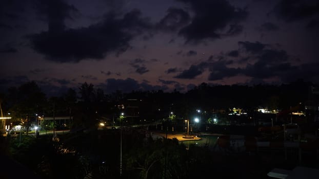 Streetlights casting a warm glow over a deserted water park at dusk, highlighting dramatic clouds and vibrant sunset colors painting the sky, creating a serene evening atmosphere