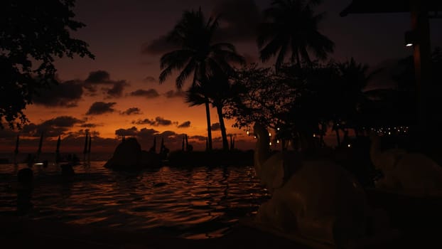 Elephant statues provide a unique foreground element to a stunning tropical sunset reflected in the tranquil waters of a resort pool, creating a serene and exotic ambiance