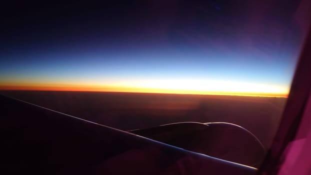 Airplane wing soaring through the atmosphere, offering a breathtaking view of the sun setting below the horizon, casting vibrant hues of orange and yellow across the sky