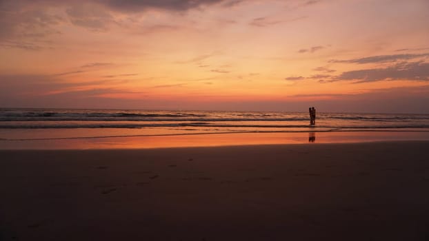 Golden hour paints the sky and ocean in warm hues as a couple embraces in the shallow water, creating a serene and romantic scene on a tropical beach