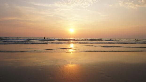 Tourists basking in the warm glow of the setting sun, enjoying the last rays of daylight while swimming in the ocean, surrounded by a stunning golden sunset reflecting on the wet sand
