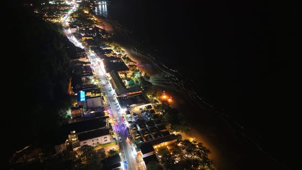Capturing a vibrant coastal road at night, illuminated buildings, bustling traffic, and the dark ocean create a striking contrast between land and sea