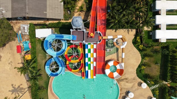 Aerial view captures the vibrant and exciting atmosphere of a water park, with colorful waterslides twisting and turning around pools and amidst lush tropical greenery
