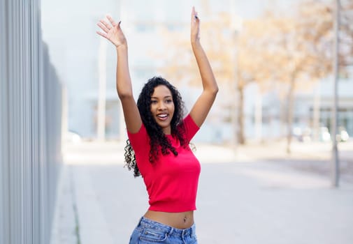 A vibrant, energetic young woman wearing a stylish pink top joyfully and confidently poses outdoors, capturing the essence of positivity, selfexpression, and freedom in a lively modern urban setting