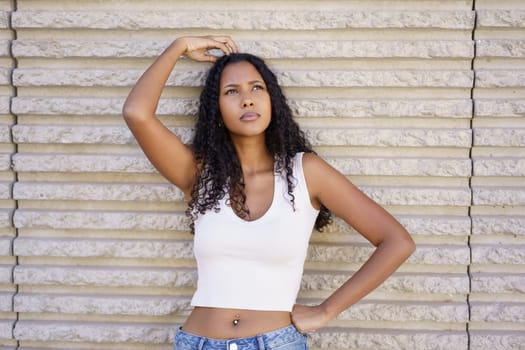 A woman with beautifully styled curly hair poses thoughtfully against a textured wall, which beautifully accentuates her expressive stance and unique sense of fashion, capturing a moment of elegance
