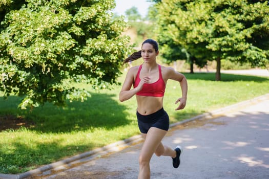 In a verdant park, a woman in athletic attire runs, displaying her dedication to fitness and health under the sun, embodying keywords like exercise, wellness, and outdoor activity