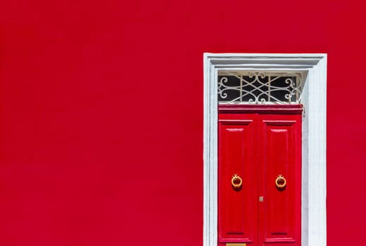 Minimalist architectural photography. Red wall of residential building facade with red door in white wooden frame.