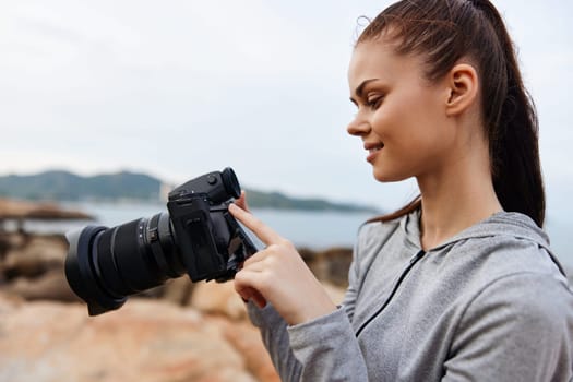 A young woman wearing a gray hoodie captures beautiful moments with her DSLR camera at the beach during sunset, blending passion and photography