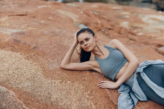 An athletic young woman rests on natural rock formations, portraying a sense of tranquility and health This image emphasizes fitness, nature, and relaxation, ideal for promoting active living and wellness