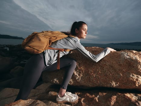 Determined young female hiker in activewear climbs a rock, embodying adventure and resilience The outdoor scene features an overcast sky and natural textures, perfect for fitness and travel themes