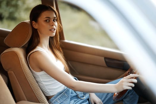 Confident young woman dressed in a simple white top and jeans, seated in a car's plush interior, capturing the essence of summer vibes and freedom on the road.