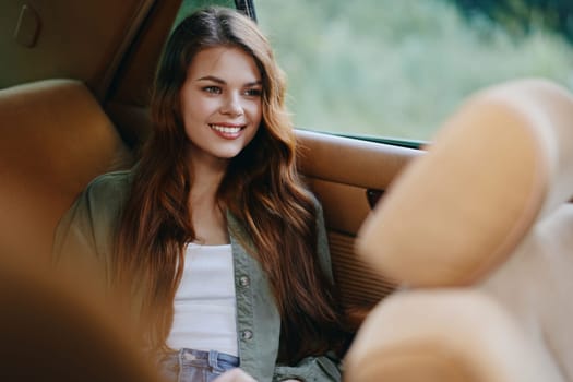 A young woman with long hair is smiling in a car, dressed in a casual green jacket and white top, surrounded by a natural outdoor background.