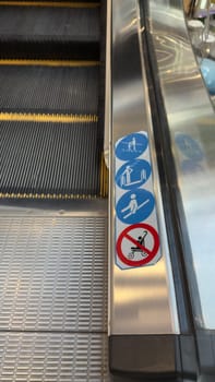 Vertical photo of escalator with sticker icons with rules of use. Safe movement on escalator with observance of rules to prevent injuries during fall on moving staircase