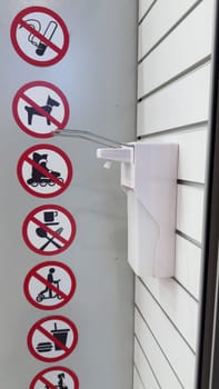 Signs with rules at entrance to store prohibiting smoking, food and drinks, use of roller skates and scooters next to antiseptic dispenser. Strict restrictions in store to ensure safety of goods