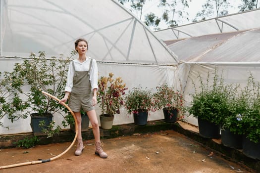 A fashionable young woman in overalls watering plants in a greenhouse, exuding a joyful and relaxed vibe This image captures the essence of gardening, nature, and a green lifestyle