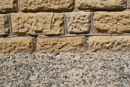 Close view of a textured stone wall with gravel at the base during daylight hours. High quality photo