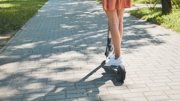 Teenager riding an electric scooter along a paved path in a vibrant park, enjoying a sunny summer day filled with leisure and freedom