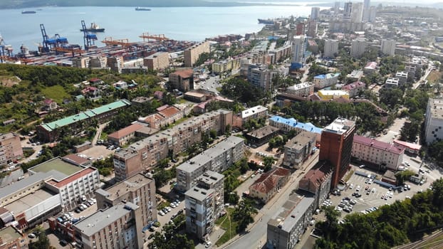 Aerial panorama revealing industrial harbor, cargo vessels approaching urban waterfront with residential high rises lining shoreline