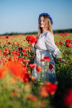 Beautiful blonde woman wearing a blue flower crown, white dress, holding a bouquet of red poppies, walking through a poppy field on a summer day
