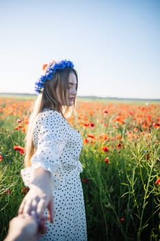 Woman with cornflower wreath walking through blooming poppy field, holding invisible partner's hand