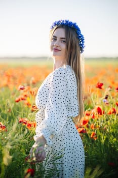 Beautiful blonde woman wearing a flower crown gently touching poppies in a field at sunset