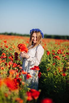 Beautiful slavic woman with flower wreath holding a bouquet of poppies in a large poppy field