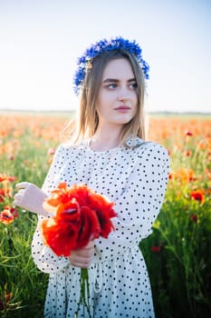 Crowned woman embracing poppy bouquet amid blooming cornflower landscape, radiant sunset illuminating golden meadow