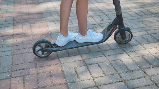 Close up of legs and feet of teen girl riding electric scooter in park during summer, enjoying sustainable transportation