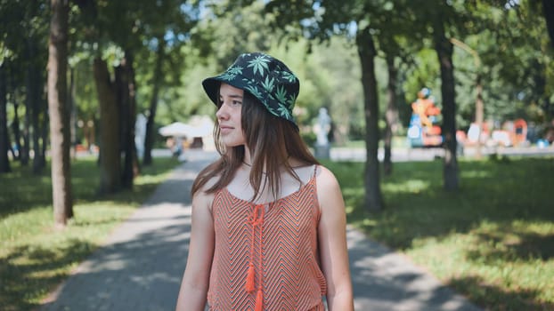 Young woman wearing a bucket hat with a marijuana leaf print enjoying a summer day in a public park