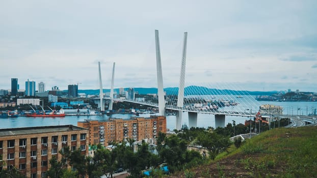 Golden stayed cable bridge spanning golden horn bay, featuring cargo vessels, vladivostok urban skyline, primorsky krai, russia