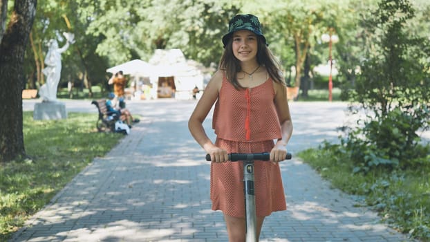 Young teen navigating electric scooter through sunny park, beaming with joy during outdoor recreation