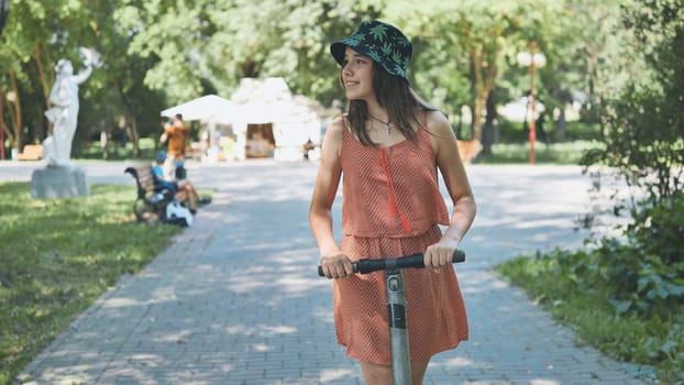 Woman riding electric scooter through sunny park, experiencing eco friendly urban mobility with carefree attitude