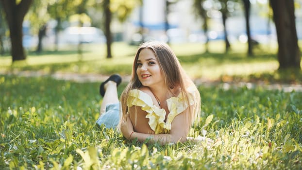 Happy young woman lying on lush green grass in a park, soaking up the summer sun and enjoying a peaceful day in nature