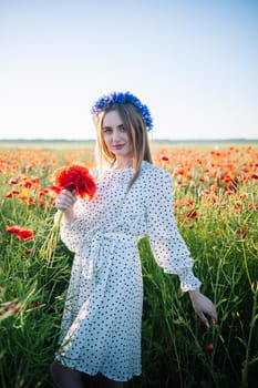 Beautiful blonde woman wearing a blue flower crown holds a bouquet of poppies in a field of poppies