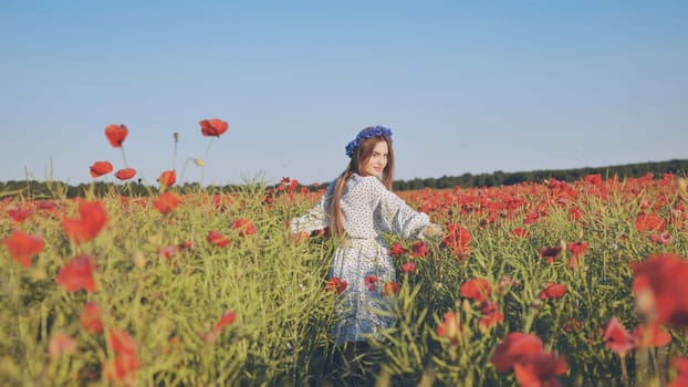 Beautiful young woman with long hair wearing a flower wreath walking in a poppy field on a sunny summer day