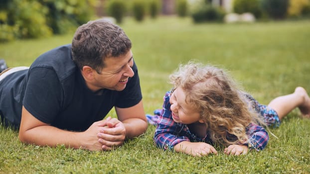 Father and daughter enjoying a playful moment together, lying on the grass and sharing laughter on a sunny day
