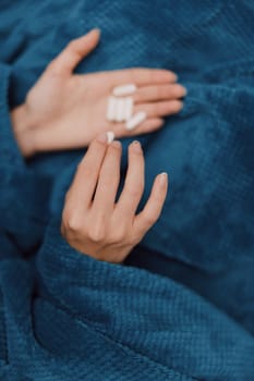 Person lying on blue blanket holding two pills in hands, one white and one blue. health concept image.