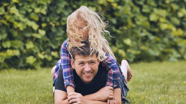 Loving father and young daughter resting on green lawn, embracing and sharing warm, tender moment together