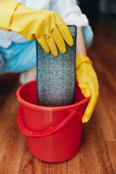 Cleaning person with rubber gloves washing floor with sponge and bucket of water. "cleaning" word is written on the bucket.
