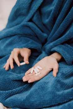 Person wrapped in blue blanket holding white pills in both hands.