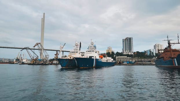 Patrol boats mooring near zolotoy bridge with vladivostok's urban landscape under gray skies, maritime infrastructure prominent