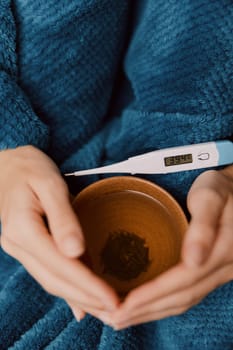 Person sitting in chair holding thermometer and cup of tea.