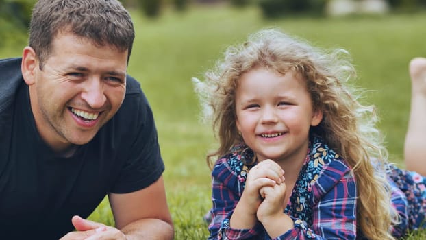 Father and daughter relaxing on grassy lawn, sharing joyful moment, laughing together under bright sunlight during outdoor family time