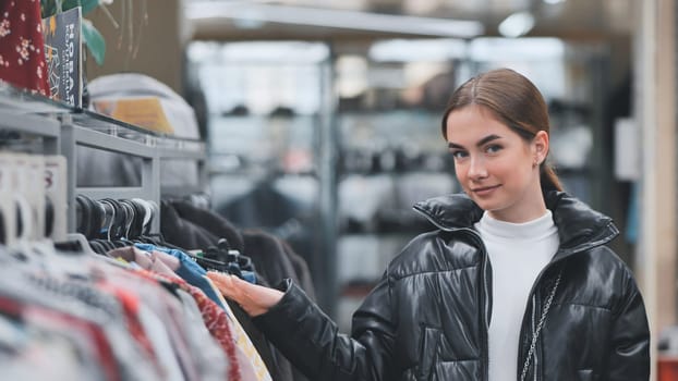 Fashion conscious woman shopping, selecting trendy apparel while moving along clothing display in retail boutique