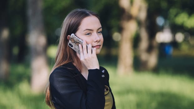 Young businesswoman making a phone call during a break in a serene park, surrounded by lush greenery and enjoying a peaceful day outdoors