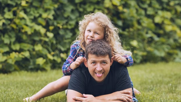 Father and daughter having fun together, lying on the grass and playfully sticking out their tongues, enjoying a summer day in their backyard