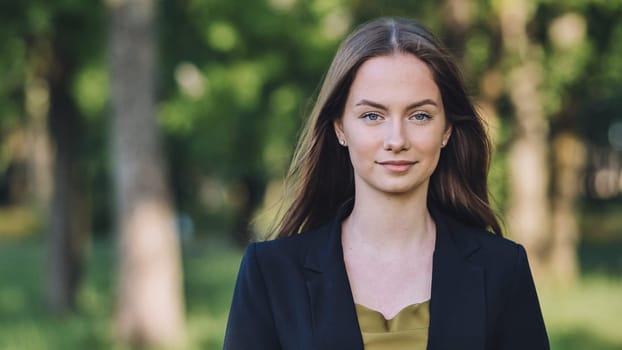 Professional businesswoman standing confidently in urban park, wearing tailored blazer and subtle smile