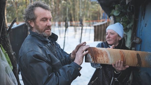 Impoverished couple navigating harsh winter, holding rusty pipe within dilapidated shantytown settlement, symbolizing economic struggle
