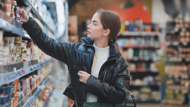 Young woman shopping groceries in supermarket, picking a product from shelf, buying food in store