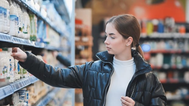 Female shopper selecting milk bottle, standing near refrigerated section in grocery store, wearing casual attire